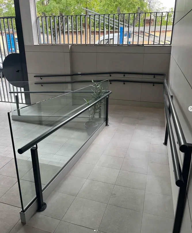 Una escalera con barandilla de cristal y una valla al fondo.