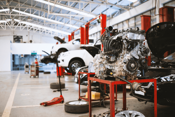 Taller mecánico con coches en elevadores, motor en soporte. Elevadores y soportes rojos.