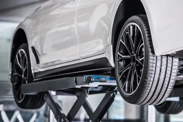 Un coche blanco elevado sobre un elevador hidráulico, dejando al descubierto sus bajos en un entorno de garaje.