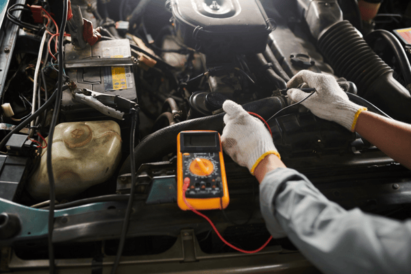 Mecánico utilizando un multímetro para diagnosticar problemas del motor del coche bajo el capó.
