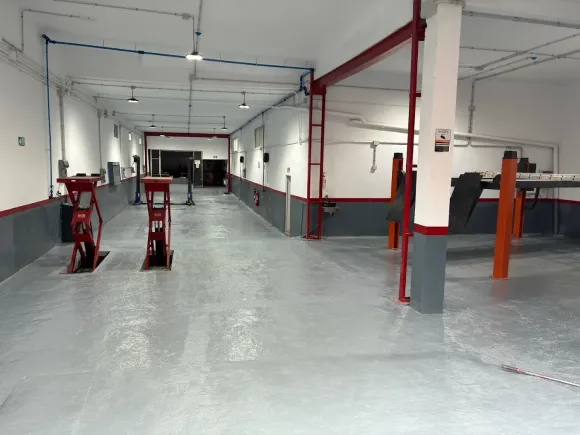 Interior espacioso de un taller de reparación de automóviles con equipamiento, iluminación brillante y suelo gris.
