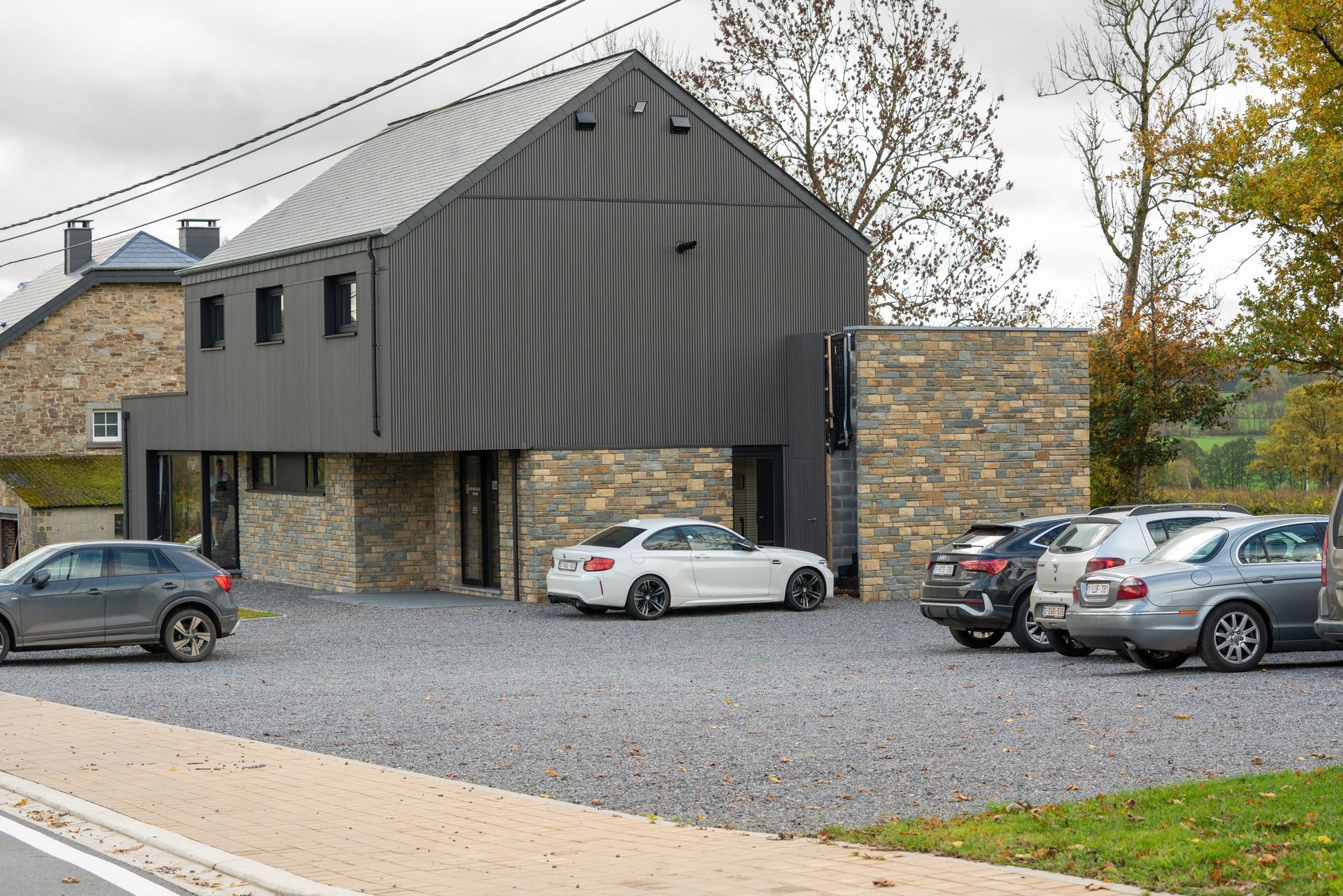 Cabinet de Kinésithérapeute moderne avec bardage gris foncé et éléments en pierre, plusieurs voitures garées devant.