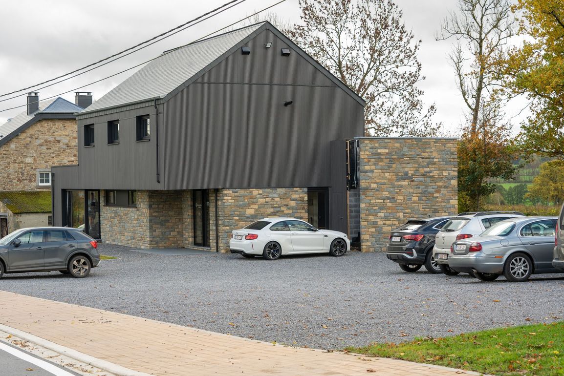 Cabinet de Kinésithérapeute moderne avec bardage gris foncé et éléments en pierre, plusieurs voitures garées devant.