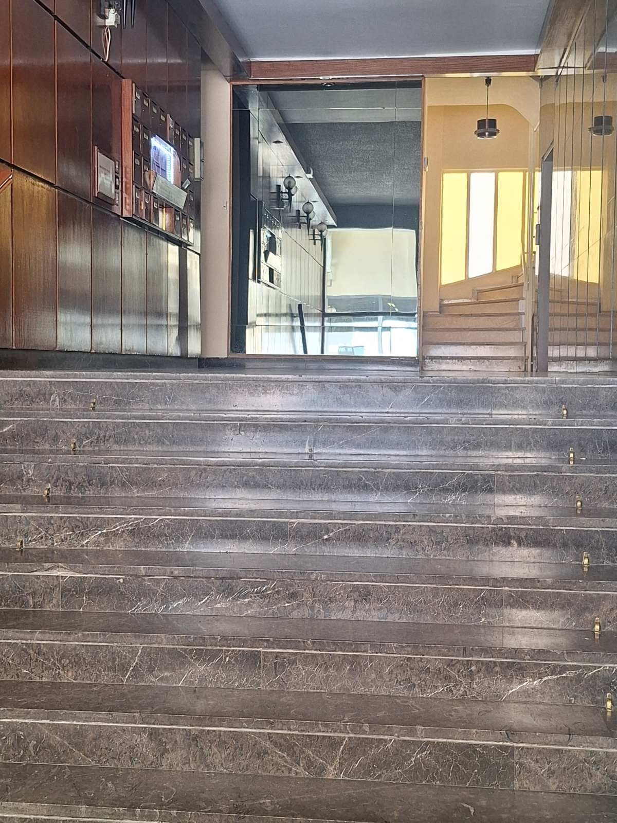 Στενή εσωτερική σκάλα με λευκά σκαλοπάτια, μπεζ τοίχους και μεταλλικό κιγκλίδωμα δίπλα σε σκούρο δάπεδο.