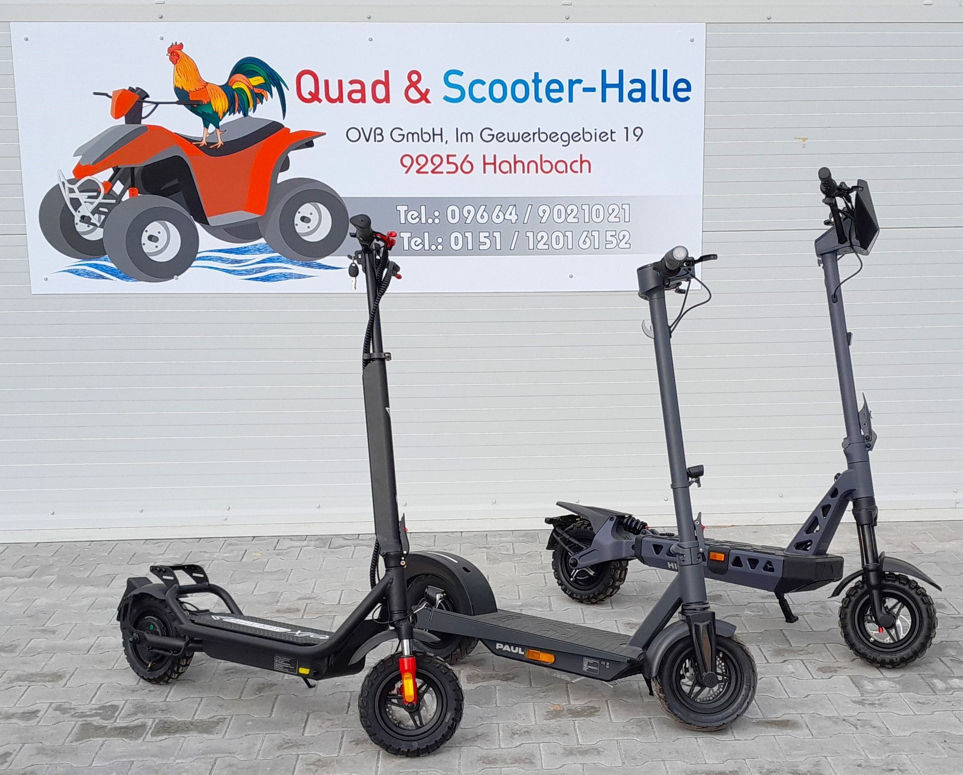 Drei Roller stehen vor einem Schild mit der Aufschrift „Quad & Scooter-Halle“