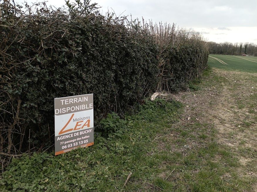 Panneau indiquant un terrain disponible avec haie et chemin de terre.