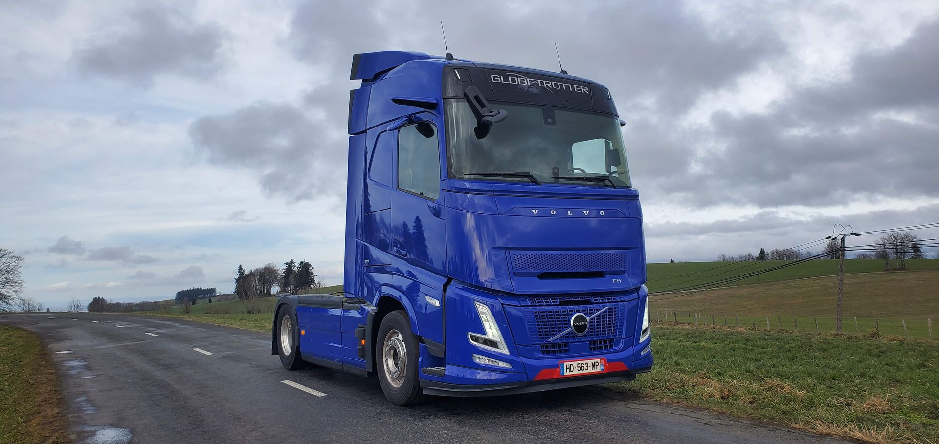 Un semi-remorque bleu est stationné au bord d'une route de campagne sous un ciel nuageux.