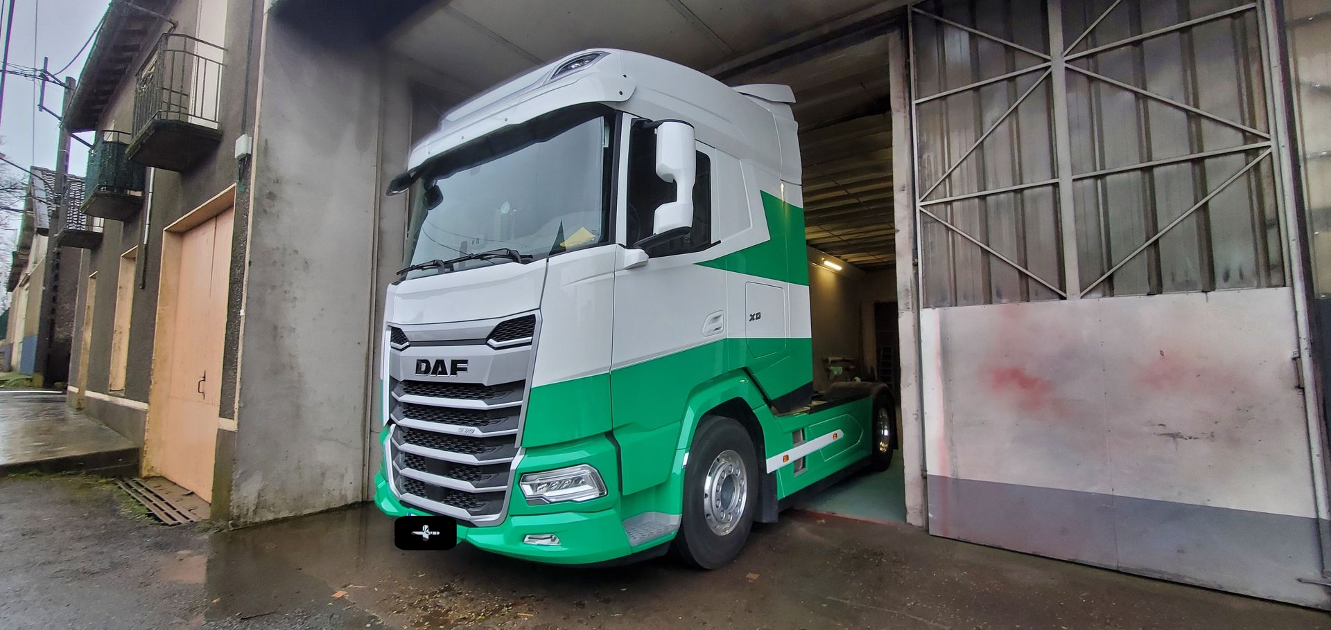 Un semi-remorque vert et blanc est garé à côté de portails métalliques.