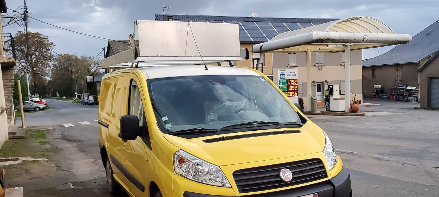 Une voiture utilitaire avec un objet sur le toit devant une station-service