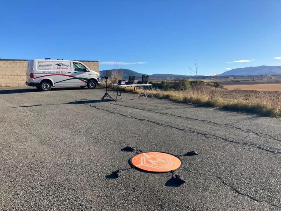 Plataforma de aterrizaje naranja para drones sobre asfalto agrietado cerca de un camión estacionado en un paisaje desértico.