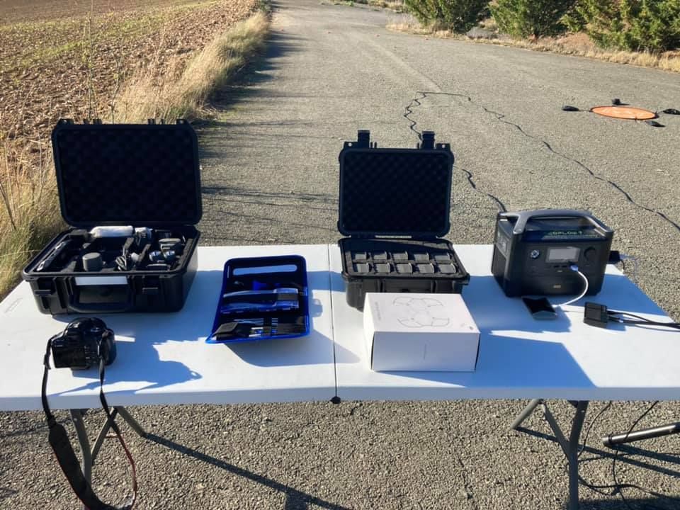 Maletines abiertos con equipos y accesorios para drones dispuestos sobre una mesa plegable al aire libre.