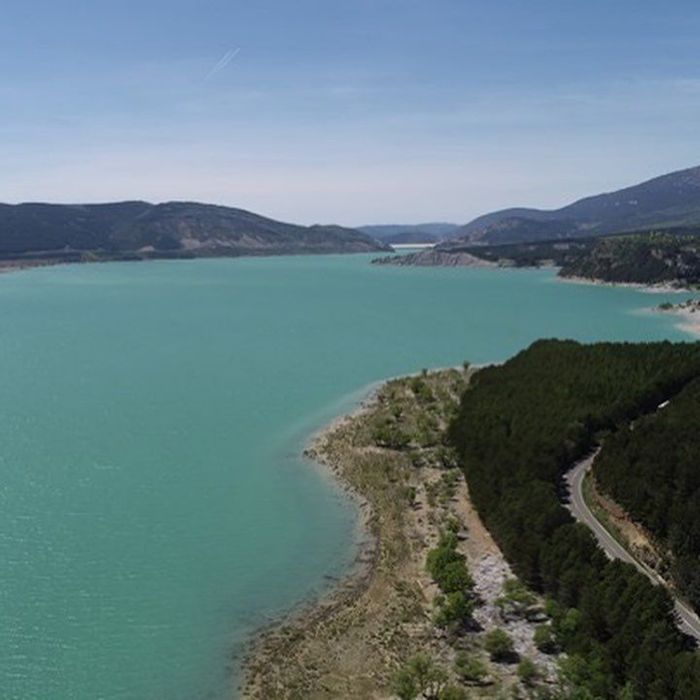 Bahía turquesa junto a una península boscosa y montañas distantes bajo un cielo despejado