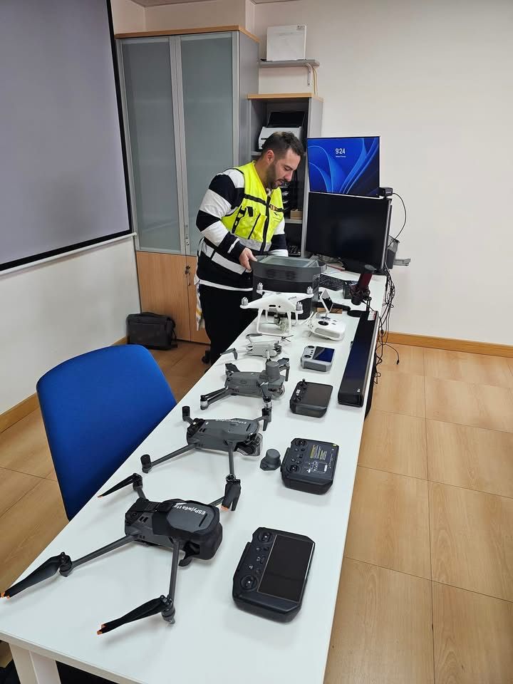 Tres personas de pie con drones en una carretera rural bajo un cielo azul y con las montañas de fondo.