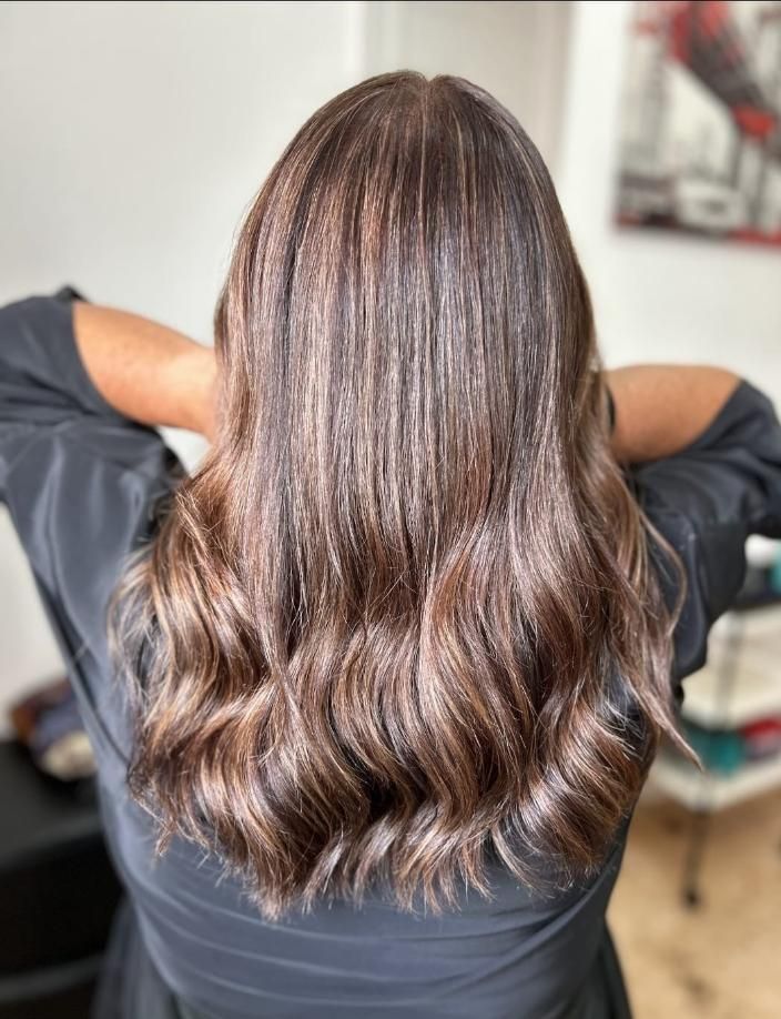 Persona con cabello largo, castaño y ondulado, vista de espaldas, vistiendo una blusa oscura.