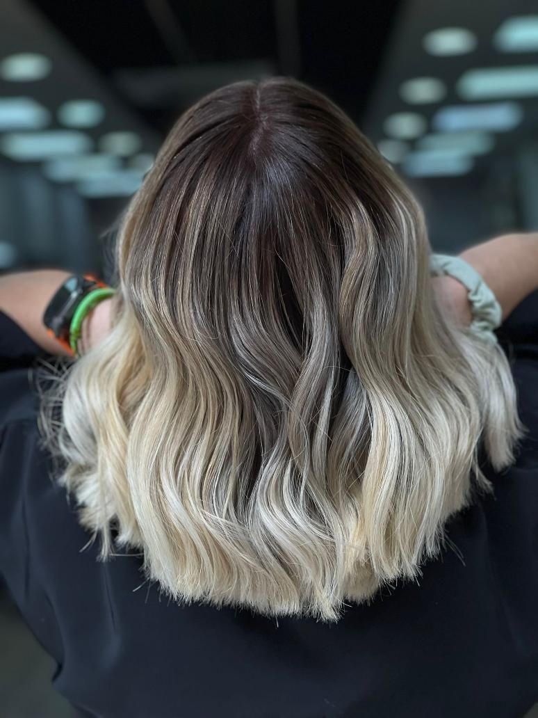 Cabello ondulado hasta los hombros con efecto ombré, desde castaño oscuro hasta rubio, visto desde atrás en una silla 