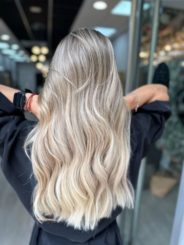 Cabello largo, ondulado y rubio platino visto desde atrás en un salón de belleza.