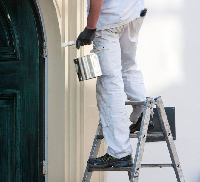 Un hombre está de pie en una escalera sosteniendo un balde de pintura.