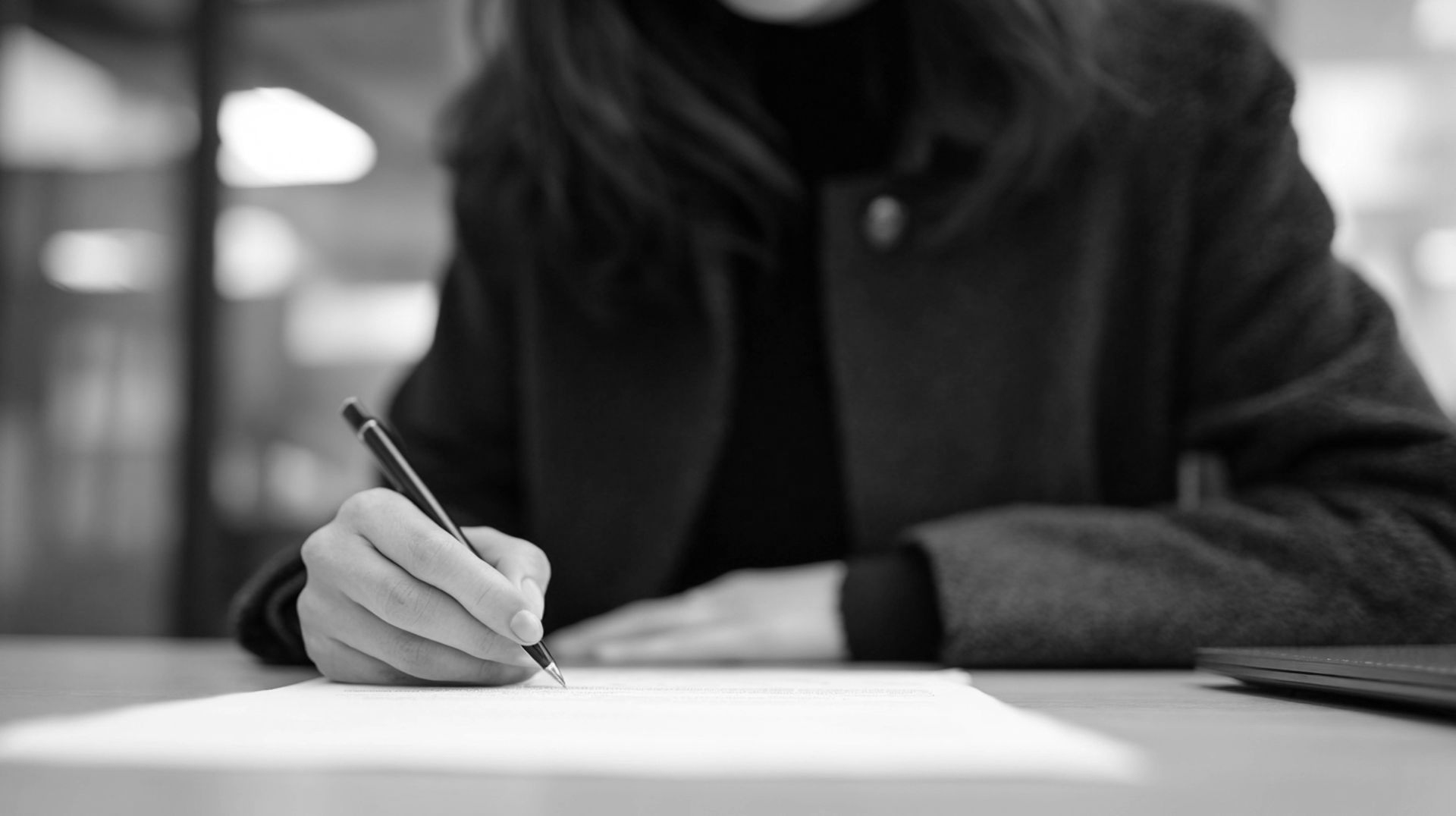 Une personne écrivant au stylo à un bureau dans un environnement de bureau en noir et blanc