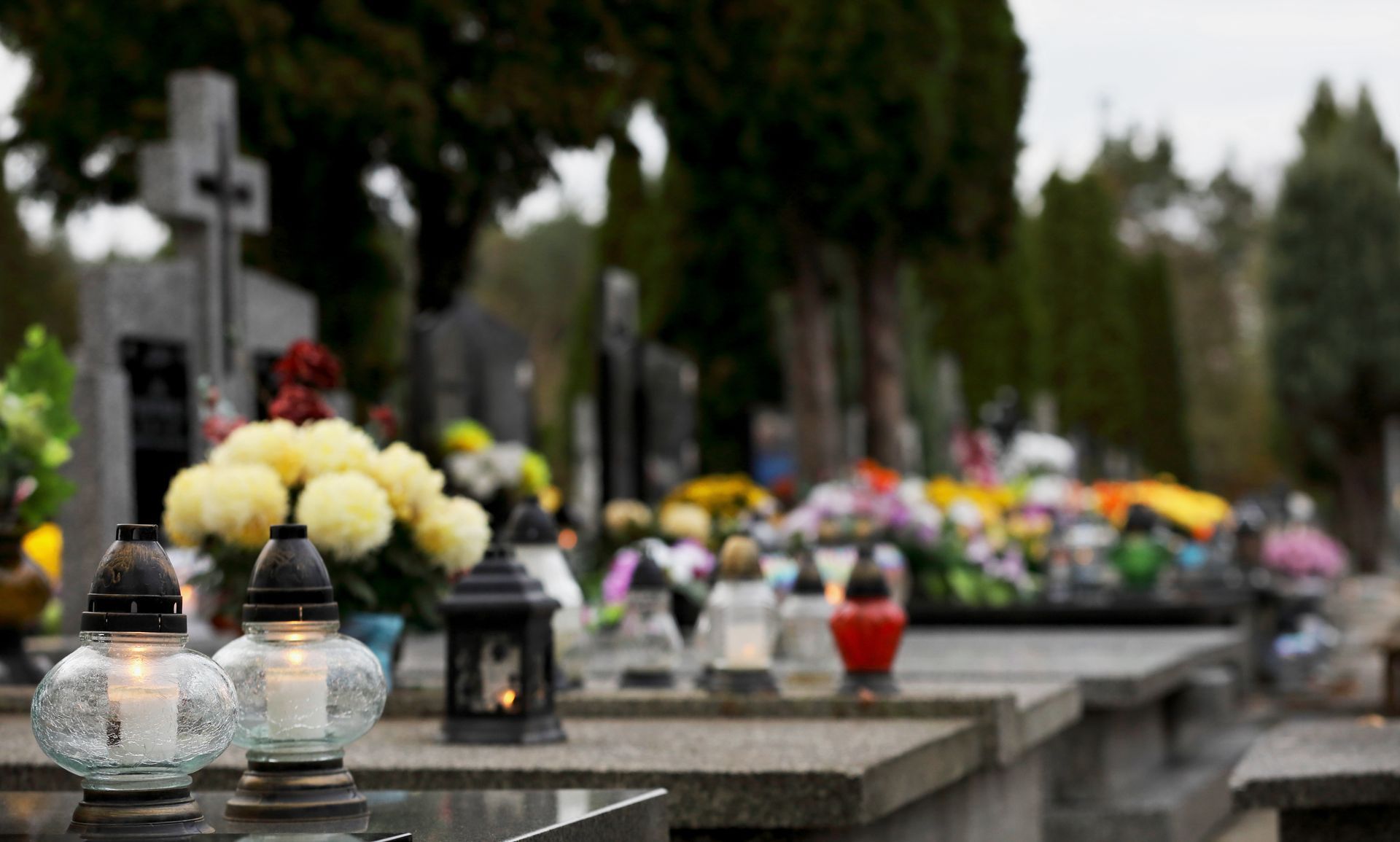 Bougies et fleurs colorées sur des tombes de cimetière, avec un arrière-plan flou bordé d'arbres.