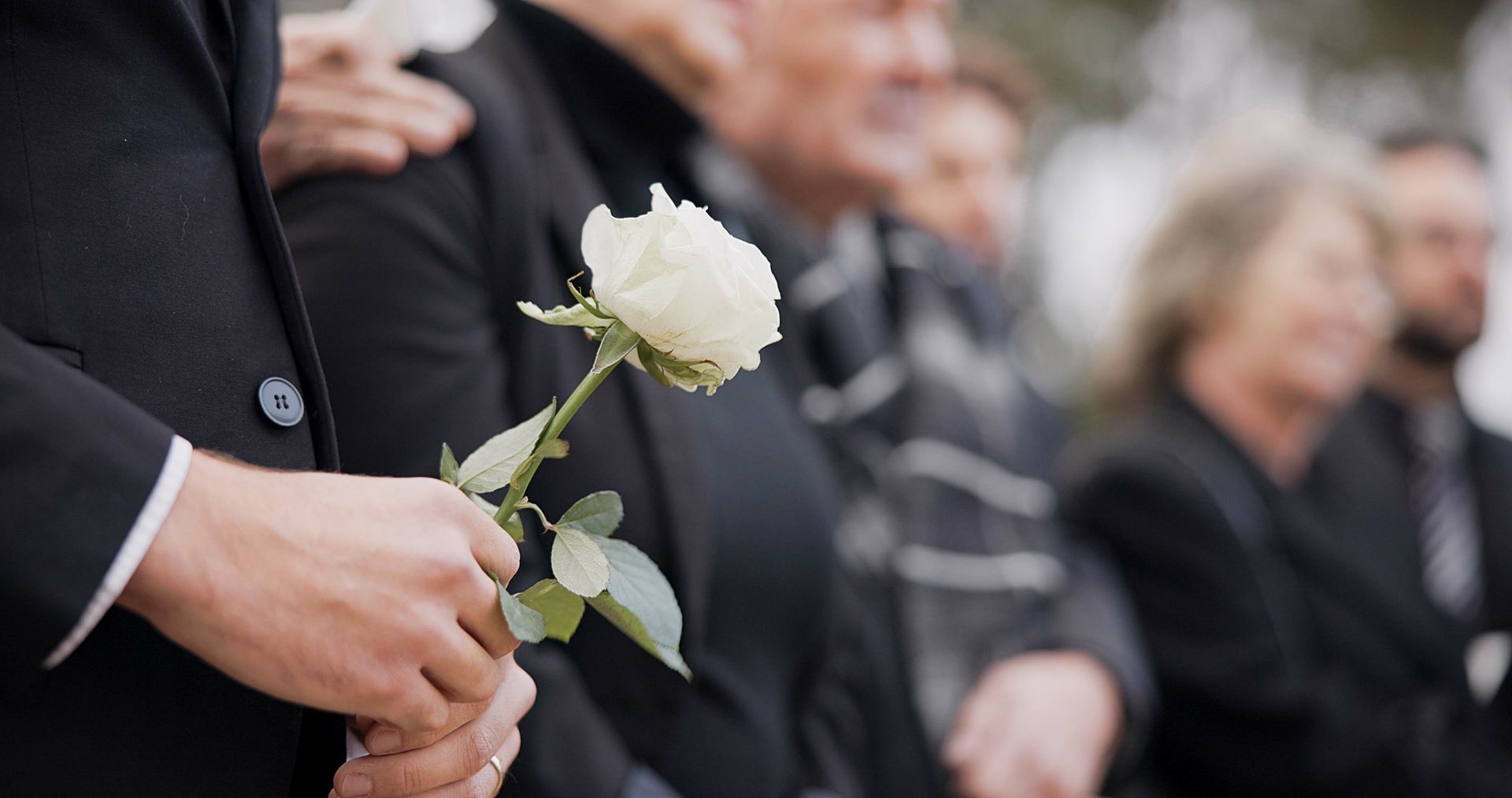Une personne tenant une rose blanche lors d'un rassemblement funéraire flou