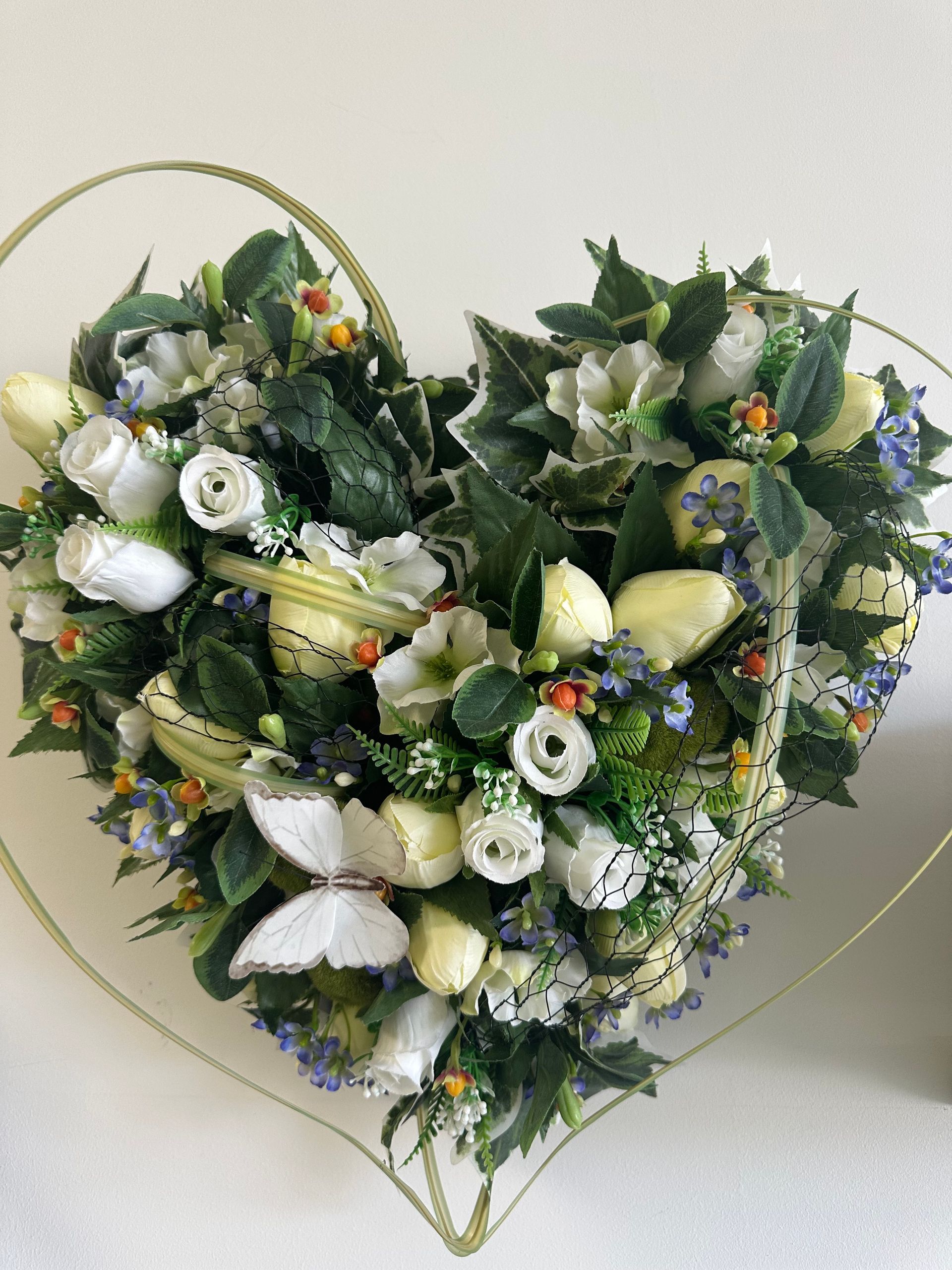 Bouquet en forme de cœur composé de fleurs blanches et de verdure sur fond clair