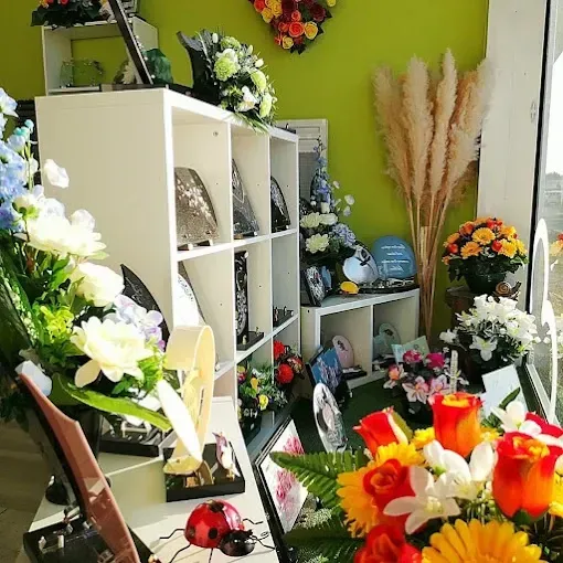 Intérieur d'une boutique de fleurs avec des bouquets colorés, des étagères blanches et de la verdure sur un mur vert citron vif.