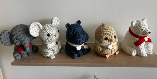Cinq figurines d'animaux crochetées alignées sur une étagère en bois contre un mur uni