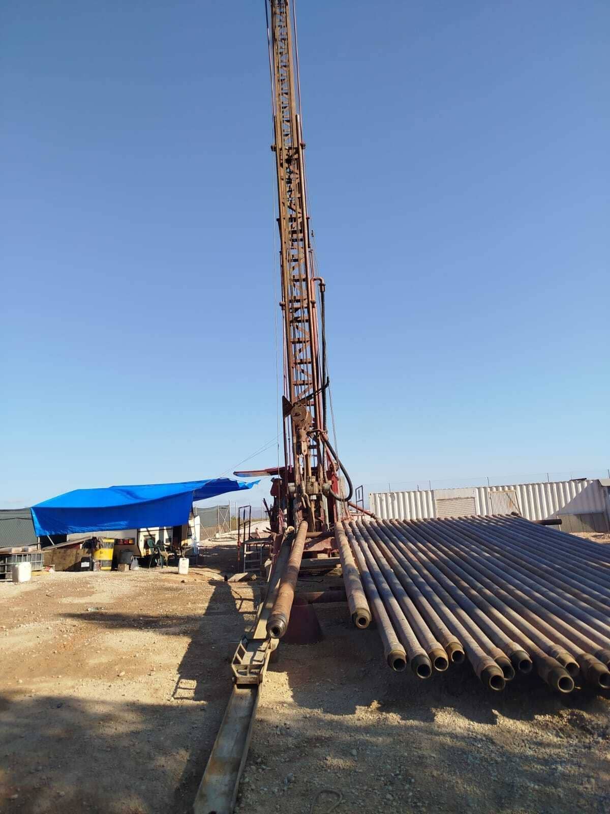 Plataforma de perforación en una obra de construcción con tuberías de acero apiladas y un refugio de lona azul bajo un cielo despejado.