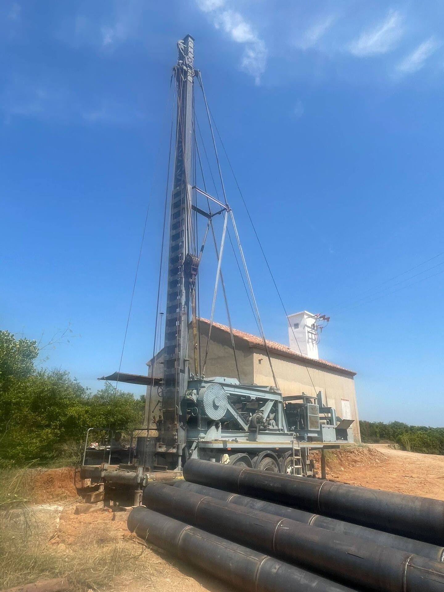 Plataforma de perforación junto a tuberías negras apiladas en un terreno baldío bajo un cielo azul despejado.