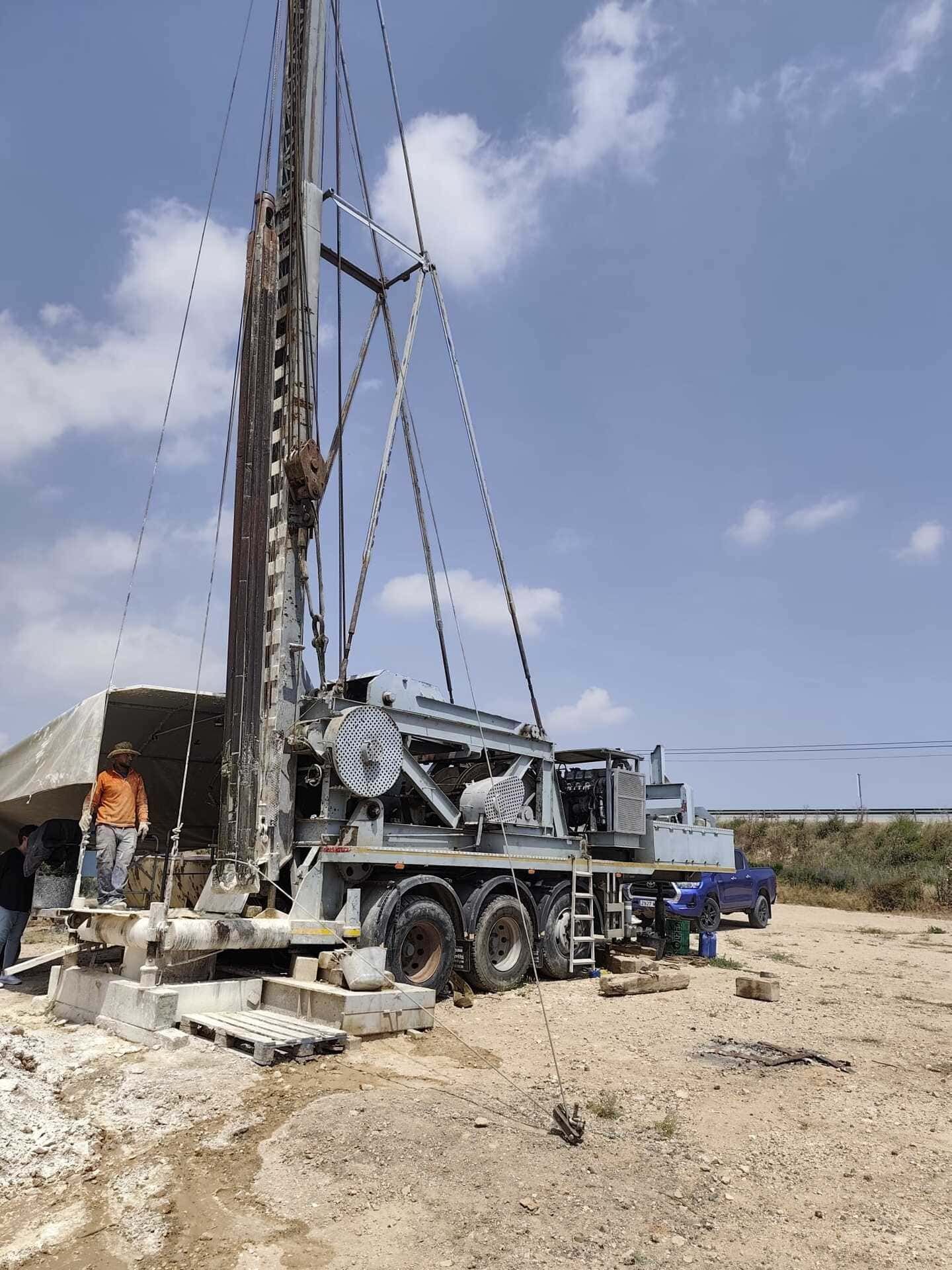 Camión perforador en una polvorienta obra de construcción bajo un cielo azul.