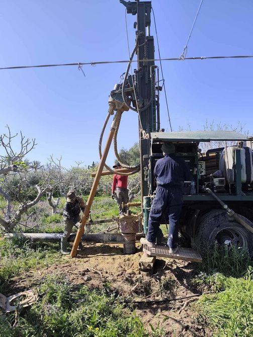 Trabajadores operando una plataforma de perforación junto a un camión en un huerto bajo un cielo azul despejado.