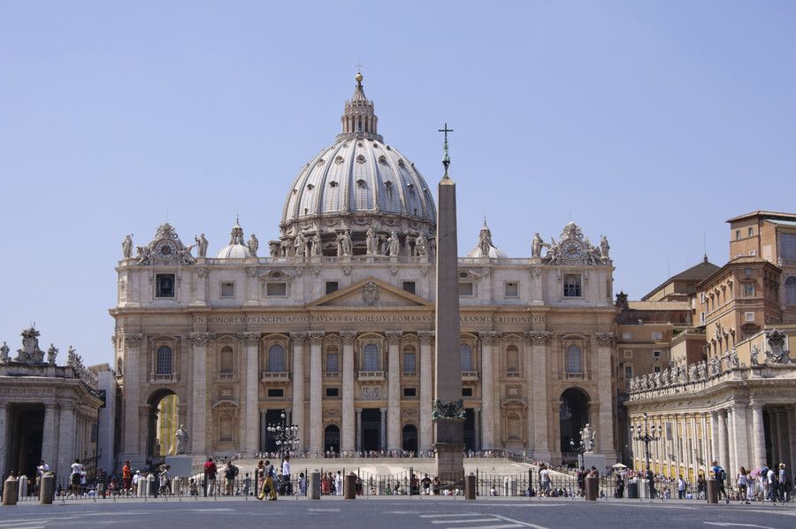 La Basílica de San Pedro en la Ciudad del Vaticano con su cúpula y plaza columnada bajo un cielo azul claro.