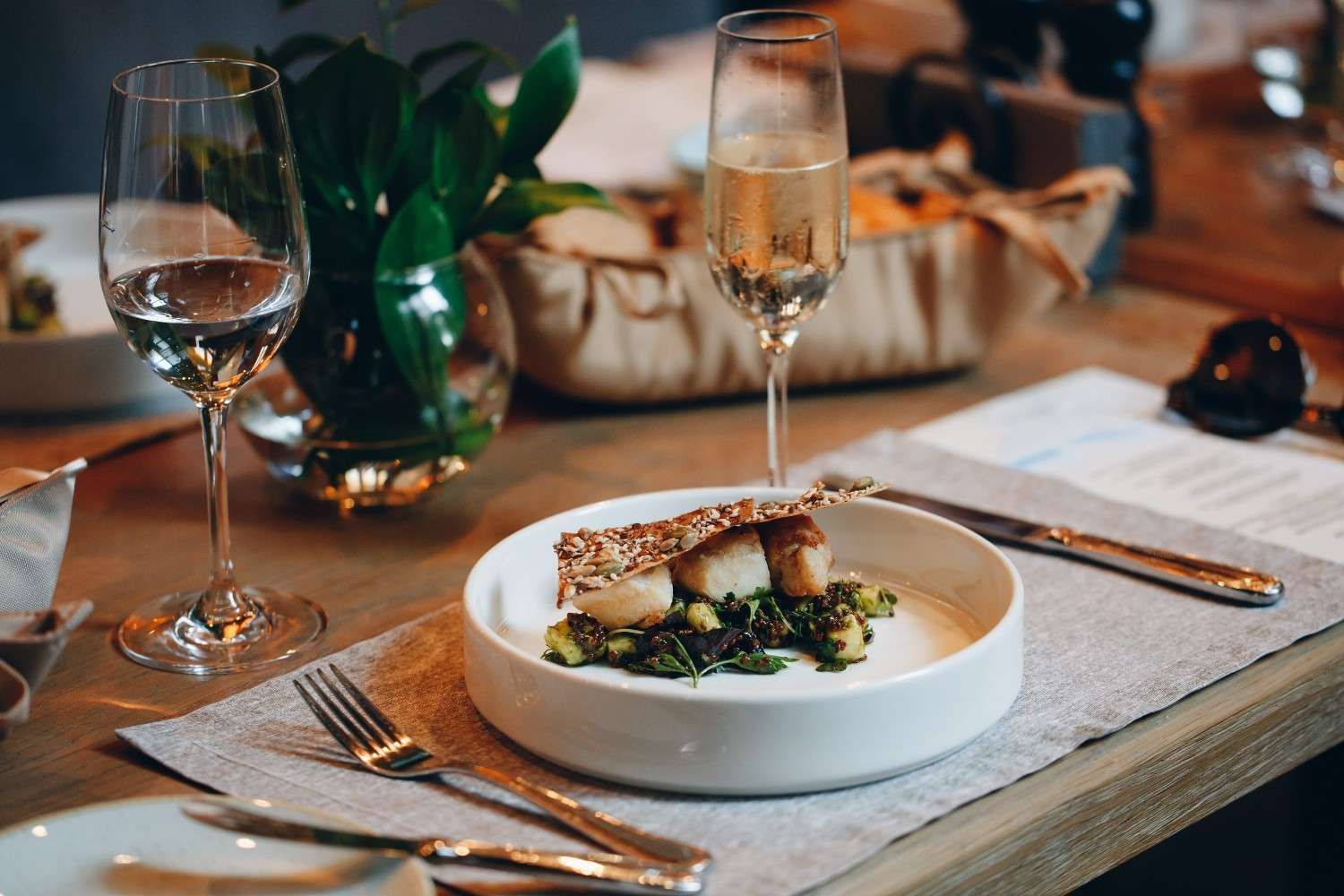 Un plato de vieiras selladas con una guarnición crujiente sobre una mesa puesta con copas de vino.