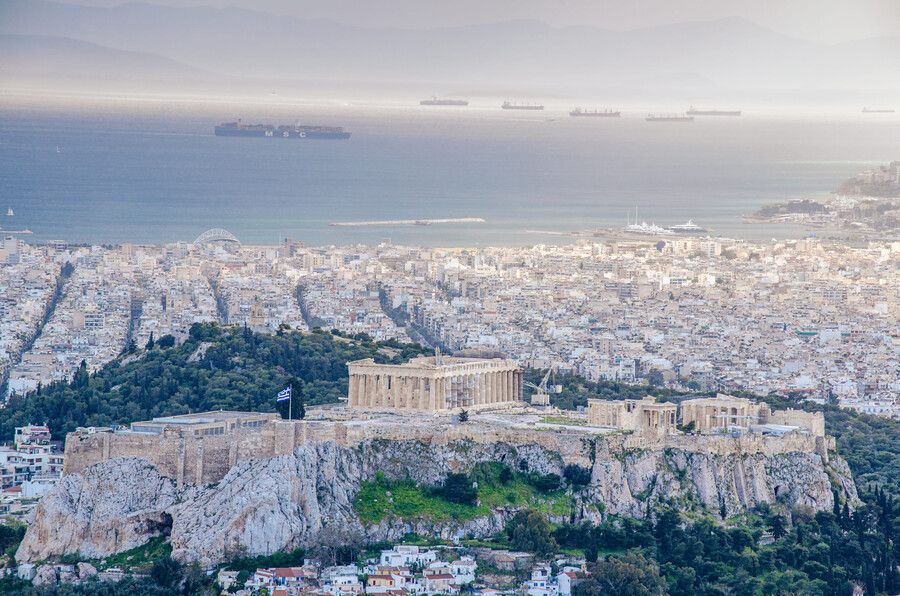 Vista de la Acrópolis en lo alto de una colina rocosa sobre Atenas, con la ciudad y el mar al fondo.