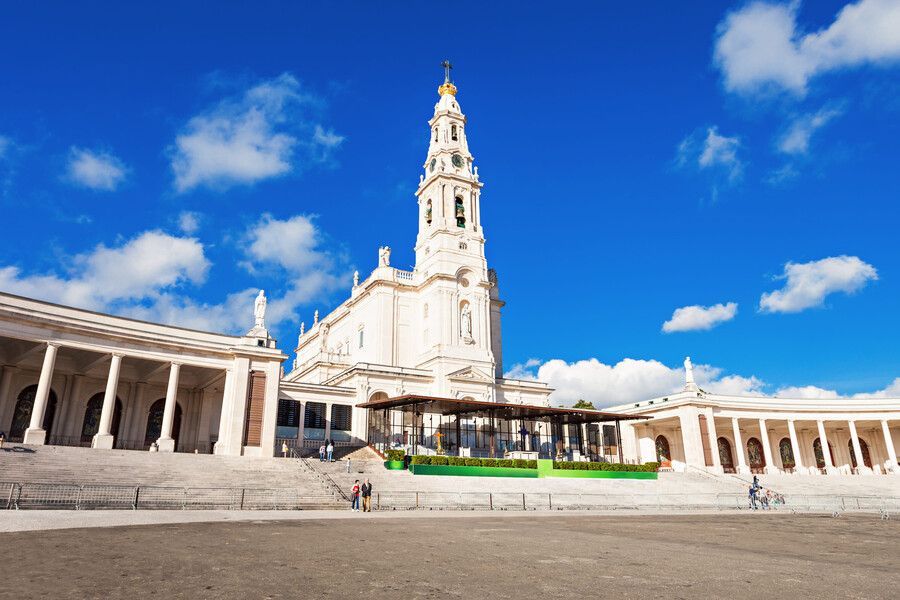 Una gran iglesia blanca con columnata bajo un cielo azul brillante con algunas nubes.