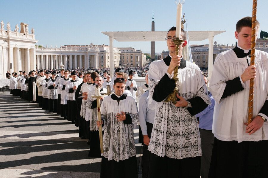 Durante una procesión religiosa, clérigos vestidos con túnicas blancas y negras forman una larga fila al aire libre.