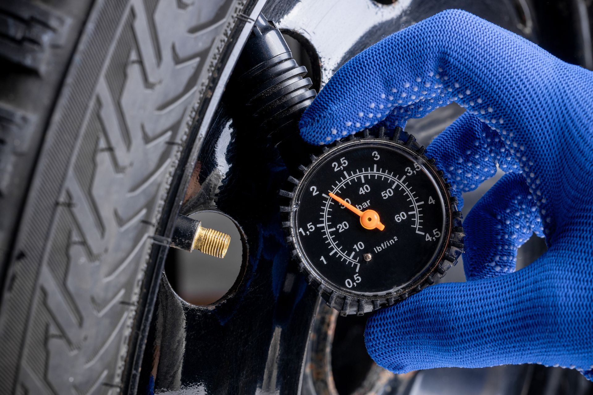 Une main gantée utilise un manomètre analogique circulaire pour vérifier la pression d'un pneu de voiture.