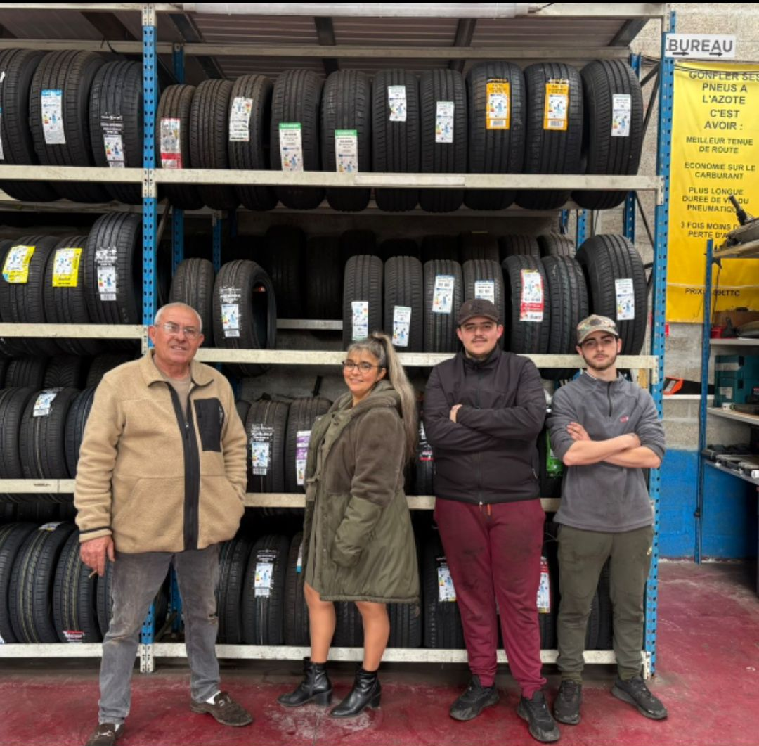 Quatre personnes posent devant des rayonnages métalliques remplis de pneus, dans un magasin de pneus.