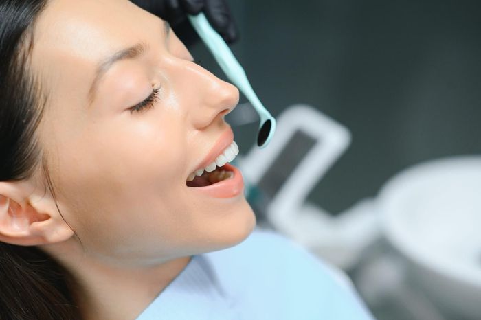 Primer plano de un paciente sonriente en la consulta del dentista, con un babero puesto y abriendo la boca durante un examen.