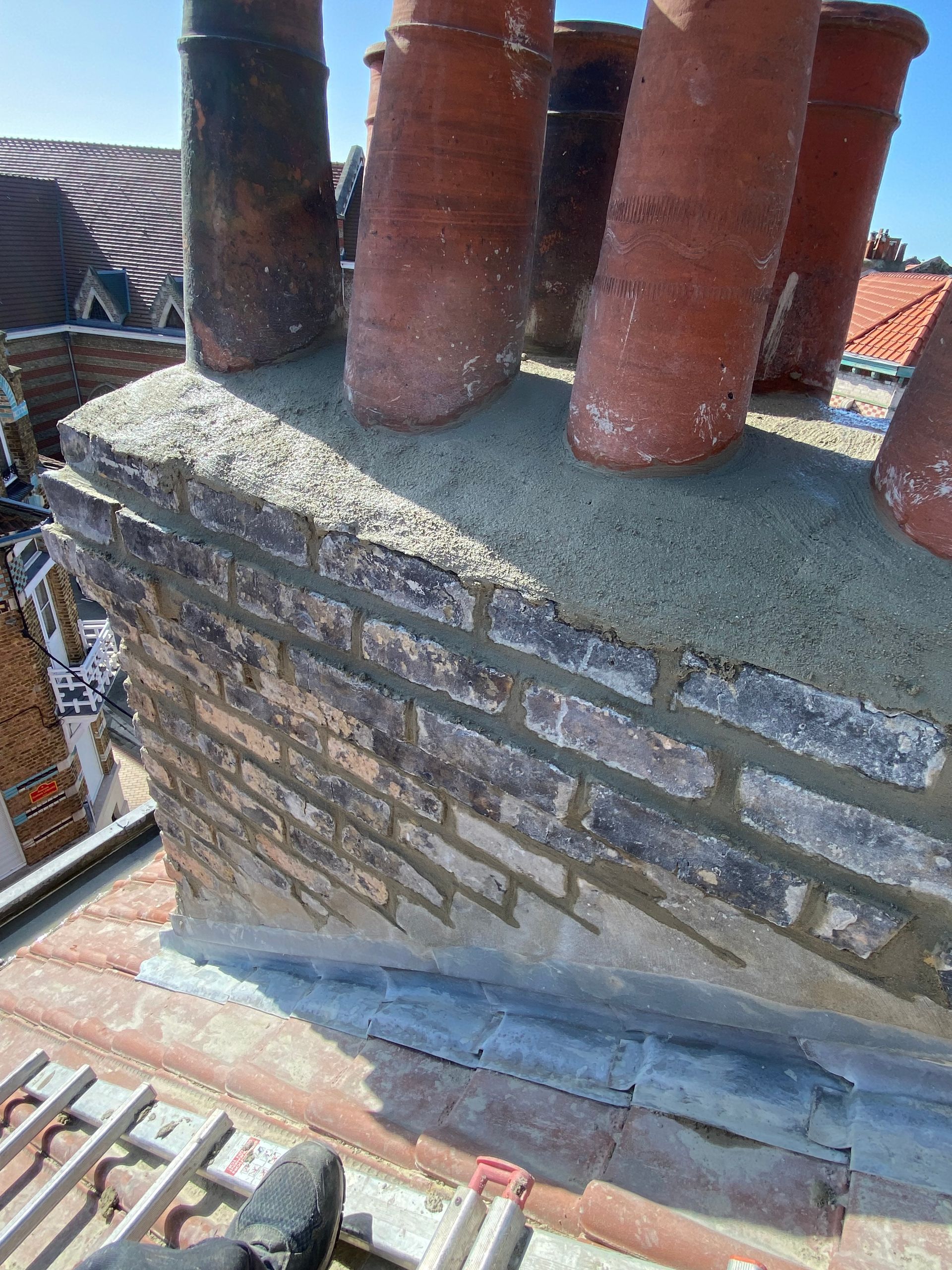 Gros plan sur une cheminée en briques sur un toit, avec des chapeaux de cheminée en terre cuite et du mortier.