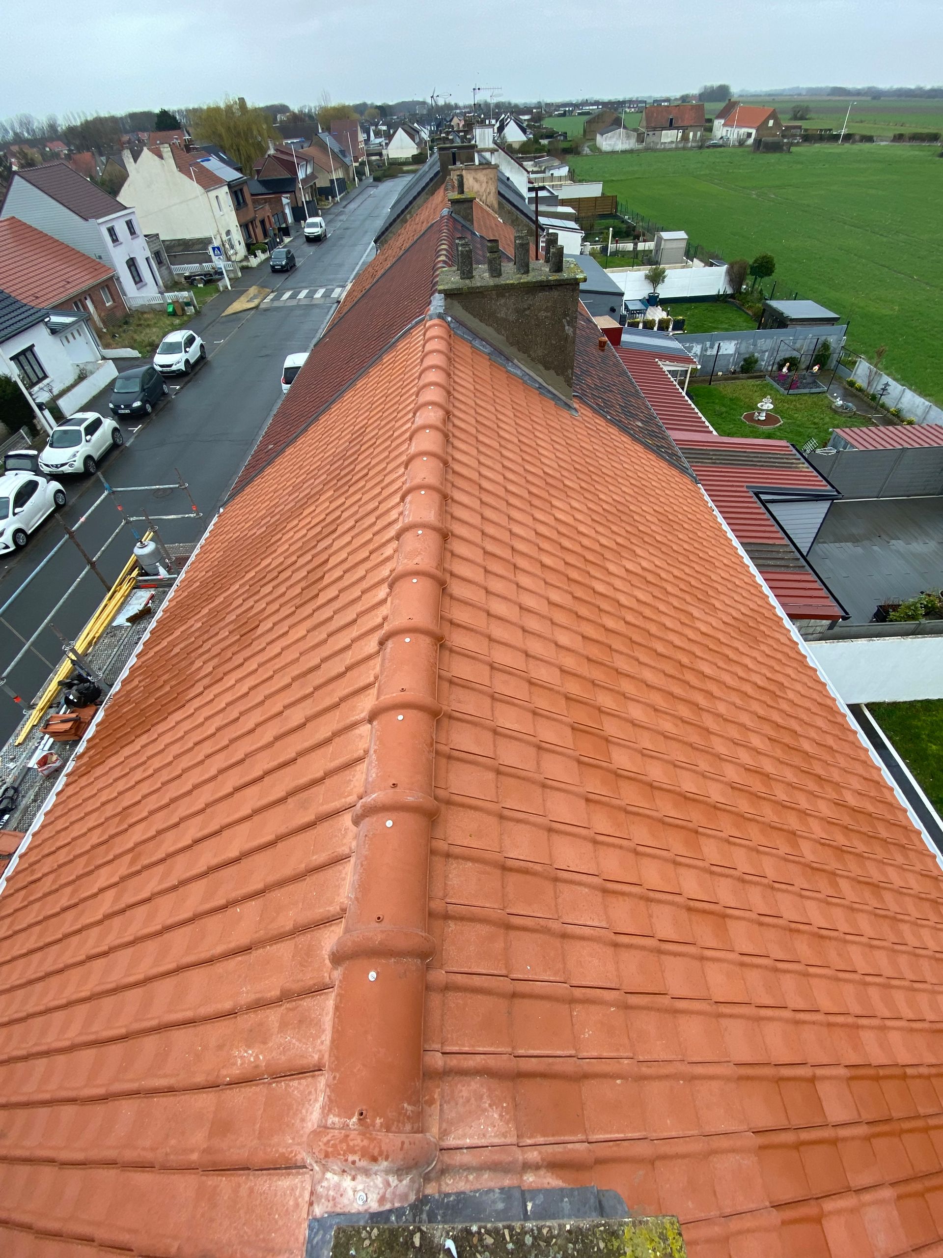Vue aérienne d'un toit de tuiles en terre cuite, avec une rue et des maisons en arrière-plan.