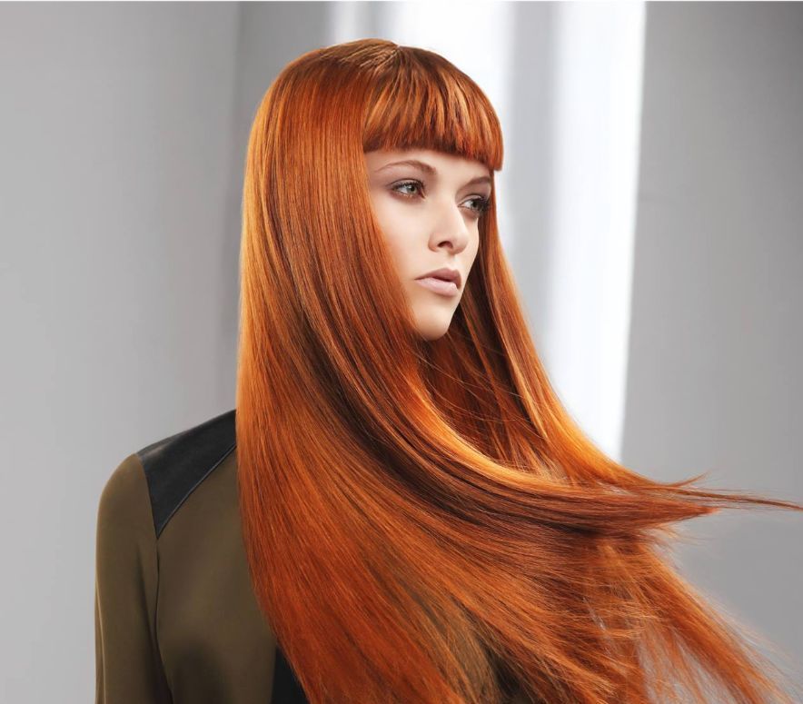 Mujer con cabello largo, liso, de color rojo brillante y flequillo recto, con un top verde y negro, mirando hacia un lado.