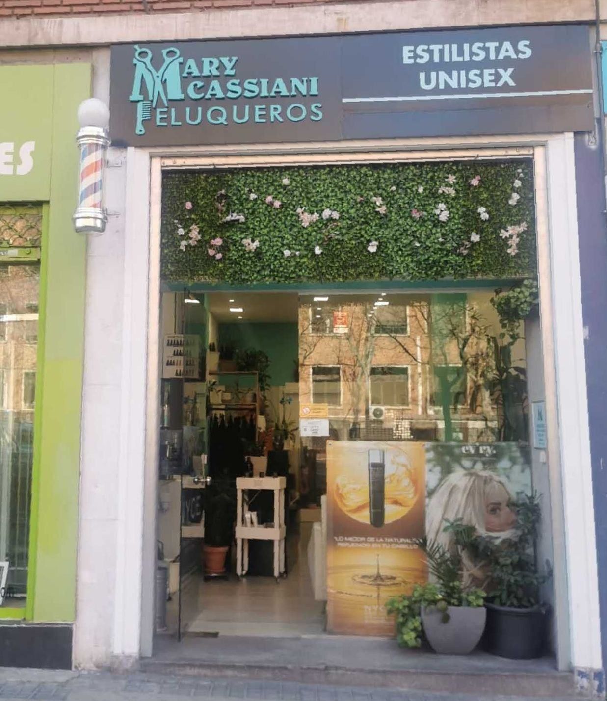 Peluquería unisex Mary Cassiani Peluqueros con poste de barbería, follaje verde y exhibiciones de productos de belleza.