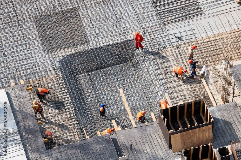 Baustelle mit Arbeitern in Sicherheitsausrüstung, Bewehrungsstahl und Holzformen für Beton.