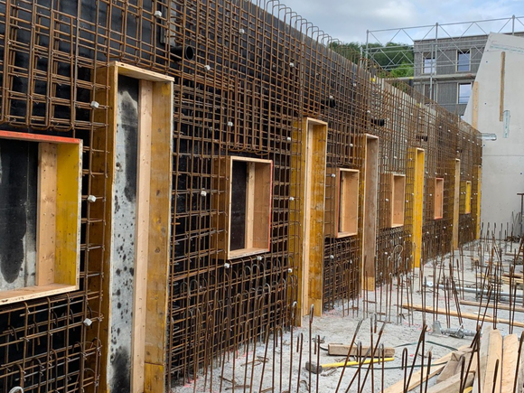 Baustelle mit Bewehrungsrahmen und Holzformen für Fenster.