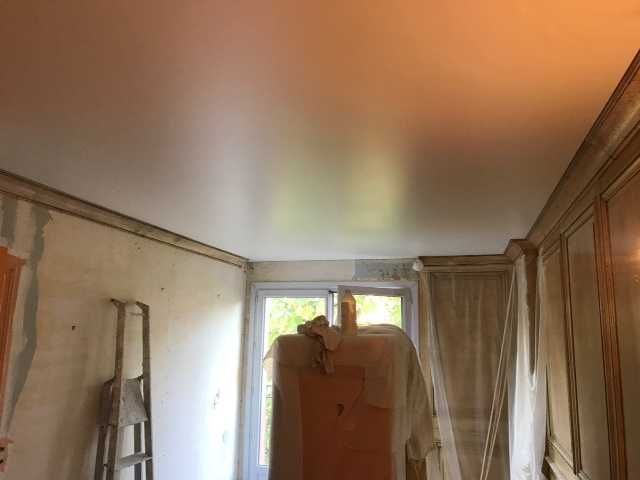 Pièce encombrée avec une échelle, un drap suspendu et une grande armoire en bois contre des murs beiges.