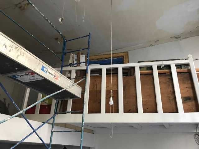 Échafaudage près d'une rambarde blanche dans une pièce inachevée où l'isolation et les plaques de plâtre sont apparentes.