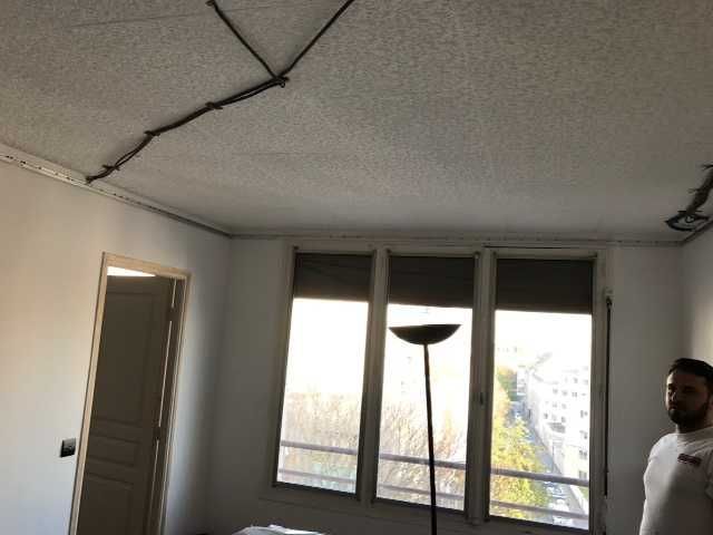 Plafond de la pièce endommagé avec des fissures, une porte, une grande fenêtre et un lampadaire près d'un homme