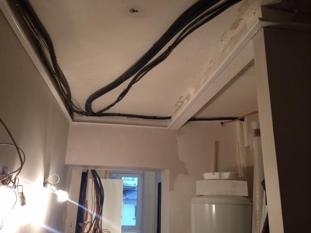 Plafond d'un couloir intérieur avec câbles noirs apparents et suspension lumineuse, vue sur une porte.