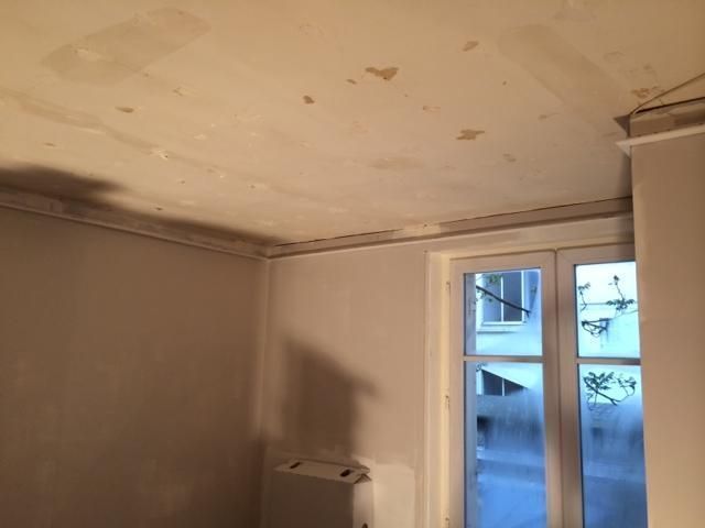 Plafond abîmé dans une petite pièce, peinture écaillée et fenêtre sur la droite